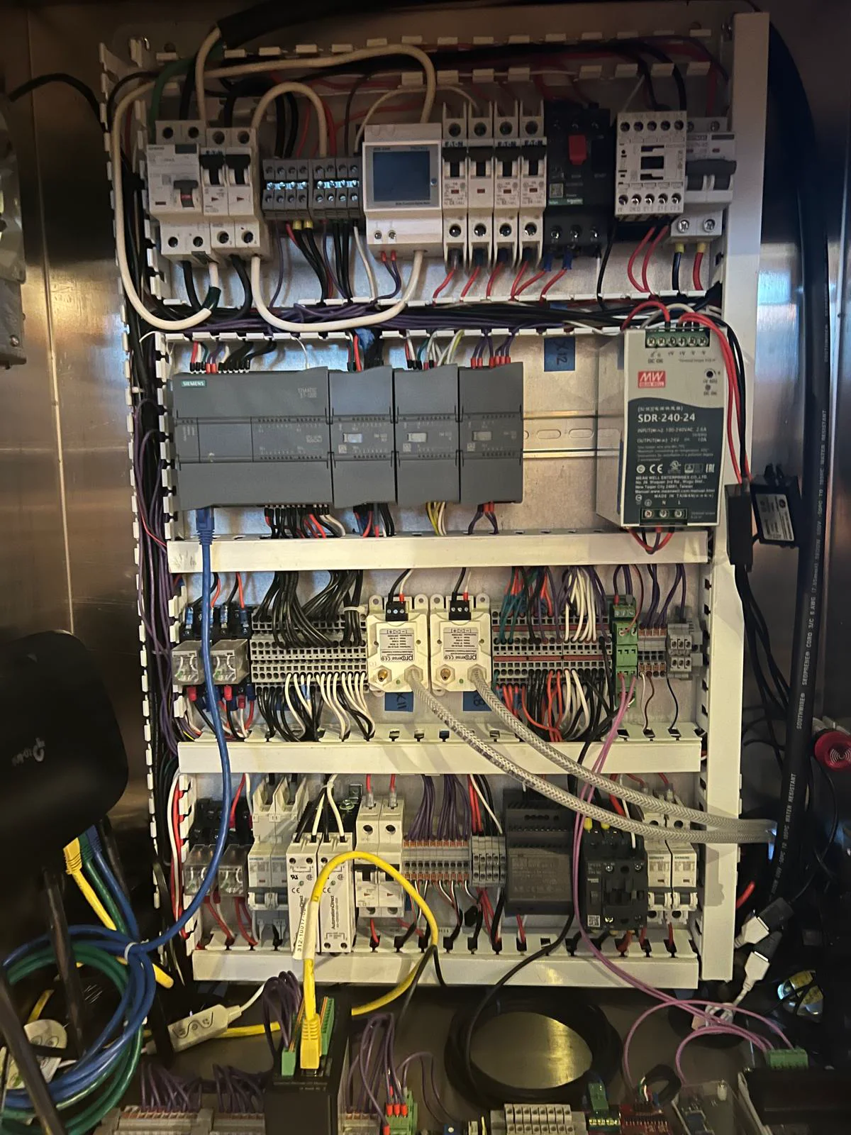 Inside an industrial control cabinet showing Siemens PLC modules, power supply, wiring, and terminal blocks